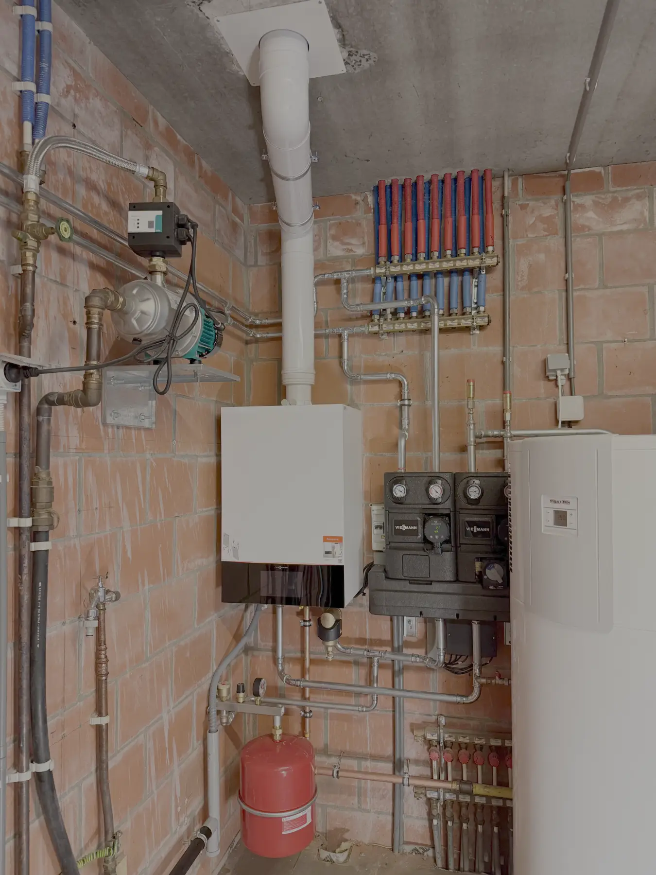 Technische ruimte met professionele cv-installatie, leidingen, verdeelgroep en warmtepomp, geplaatst door Deco-Tec uit Deinze.